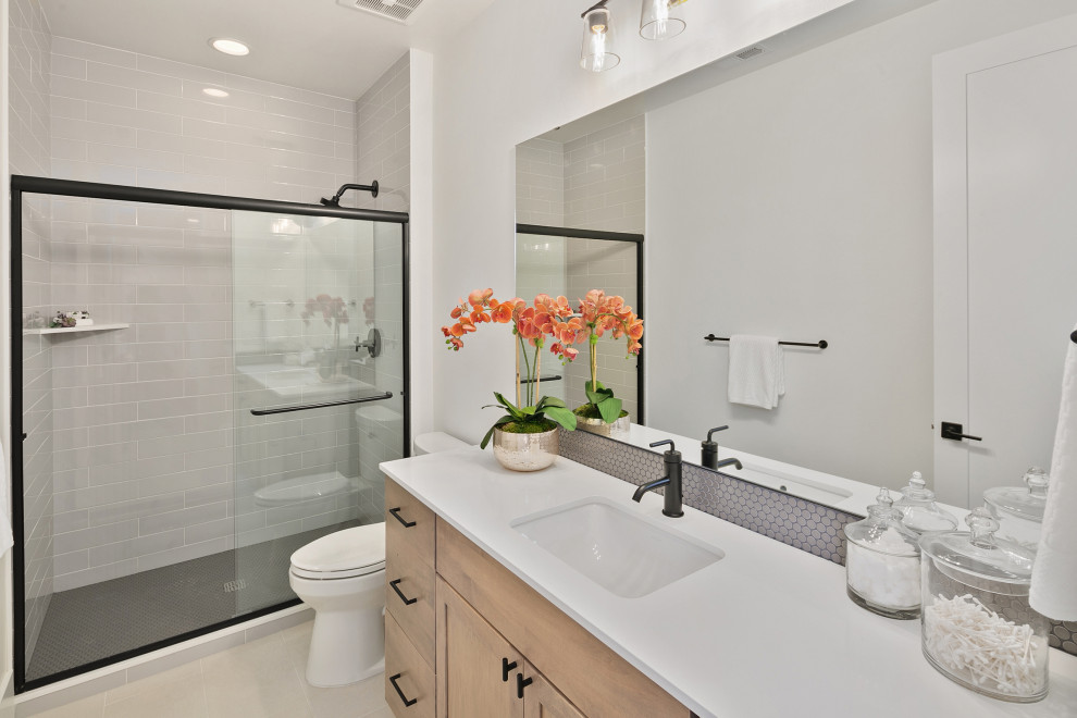 Example of a mid-sized country 3/4 gray tile and porcelain tile ceramic tile, gray floor and single-sink bathroom design in Seattle with recessed-panel cabinets, light wood cabinets, a two-piece toilet, white walls, an undermount sink, quartz countertops, white countertops and a built-in vanity