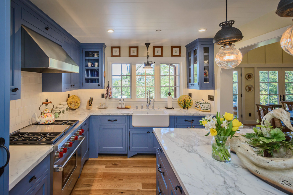 Design ideas for a mid-sized country l-shaped open plan kitchen in San Francisco with a farmhouse sink, blue cabinets, marble benchtops, white splashback, subway tile splashback, stainless steel appliances, medium hardwood floors, with island, shaker cabinets and brown floor.