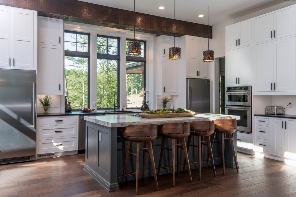 Design ideas for a large country l-shaped eat-in kitchen in Other with an undermount sink, shaker cabinets, white cabinets, granite benchtops, white splashback, window splashback, stainless steel appliances, dark hardwood floors, with island, brown floor and black benchtop.