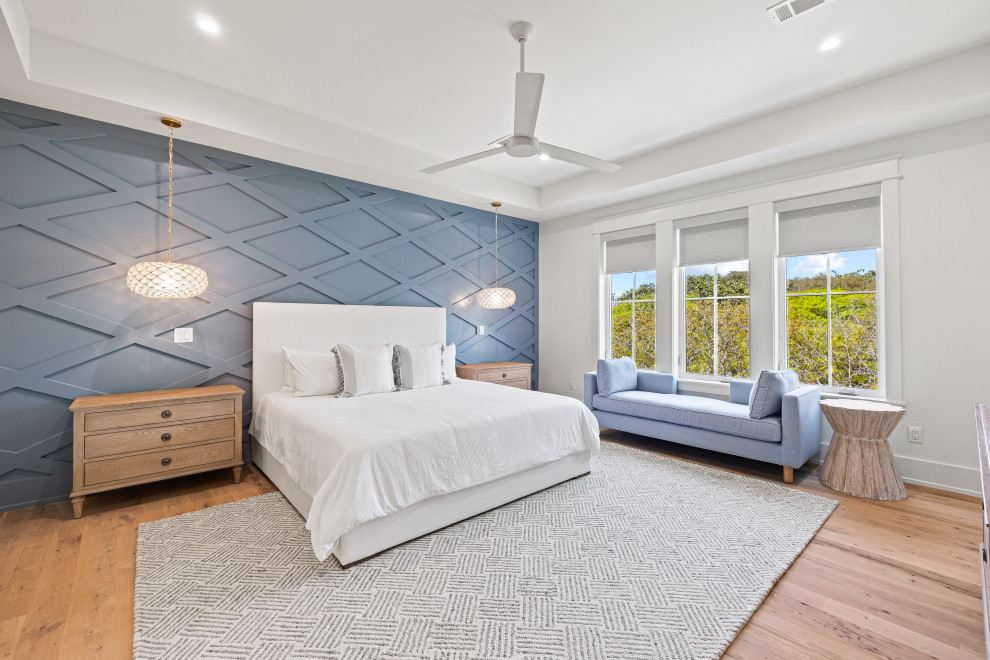 Diseño de dormitorio principal costero grande con paredes azules, suelo de madera clara y panelado