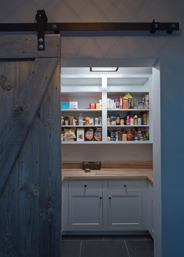 This is an example of a mid-sized country kitchen pantry in Chicago with recessed-panel cabinets, white cabinets, wood benchtops, stainless steel appliances, porcelain floors, a drop-in sink, white splashback, ceramic splashback and brown floor.