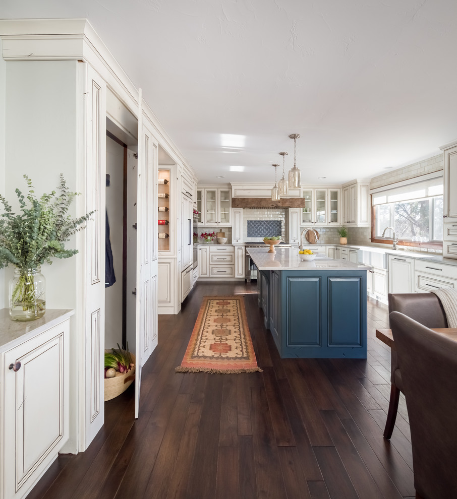 Photo of a large transitional u-shaped separate kitchen in Denver with a farmhouse sink, raised-panel cabinets, distressed cabinets, quartzite benchtops, panelled appliances, dark hardwood floors, with island, white benchtop, white splashback and brown floor.