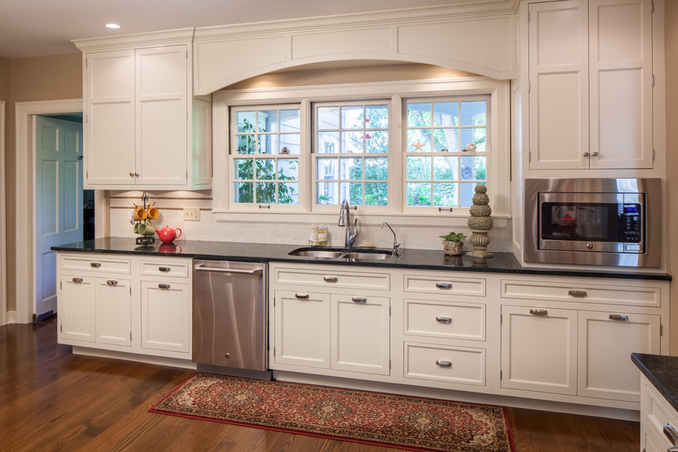 Example of a mid-sized transitional single-wall medium tone wood floor enclosed kitchen design with an undermount sink, beaded inset cabinets, white cabinets, granite countertops, white backsplash, porcelain backsplash, stainless steel appliances and no island
