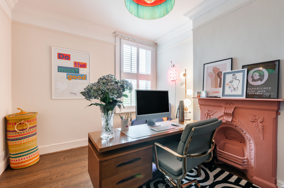 Eklektisk inredning av ett mellanstort arbetsrum, med rosa väggar, mellanmörkt trägolv, en standard öppen spis, en spiselkrans i metall, ett fristående skrivbord och brunt golv