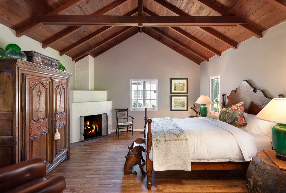 Traditional bedroom in Santa Barbara with white walls, dark hardwood floors, a corner fireplace and a brick fireplace surround.