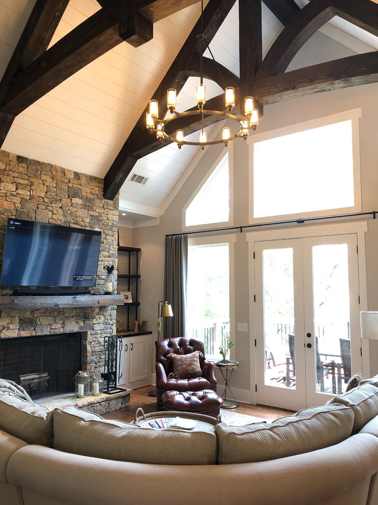 This is an example of a large country open concept living room in Atlanta with grey walls, medium hardwood floors, a wood stove, a stone fireplace surround, a wall-mounted tv and brown floor.
