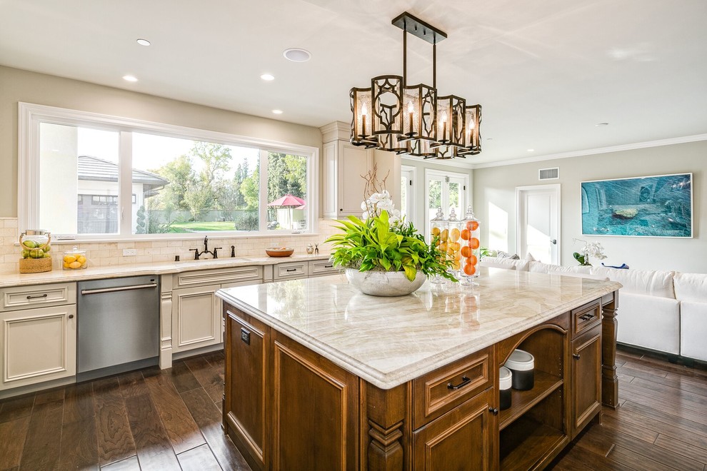 This is an example of a large traditional l-shaped open plan kitchen in Orange County with an undermount sink, recessed-panel cabinets, beige cabinets, limestone benchtops, beige splashback, subway tile splashback, stainless steel appliances, dark hardwood floors, with island and brown floor.