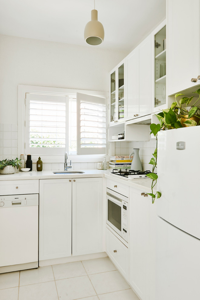Photo of a contemporary l-shaped kitchen in Melbourne with an undermount sink, shaker cabinets, white cabinets, white splashback, white appliances, white floor and white benchtop.