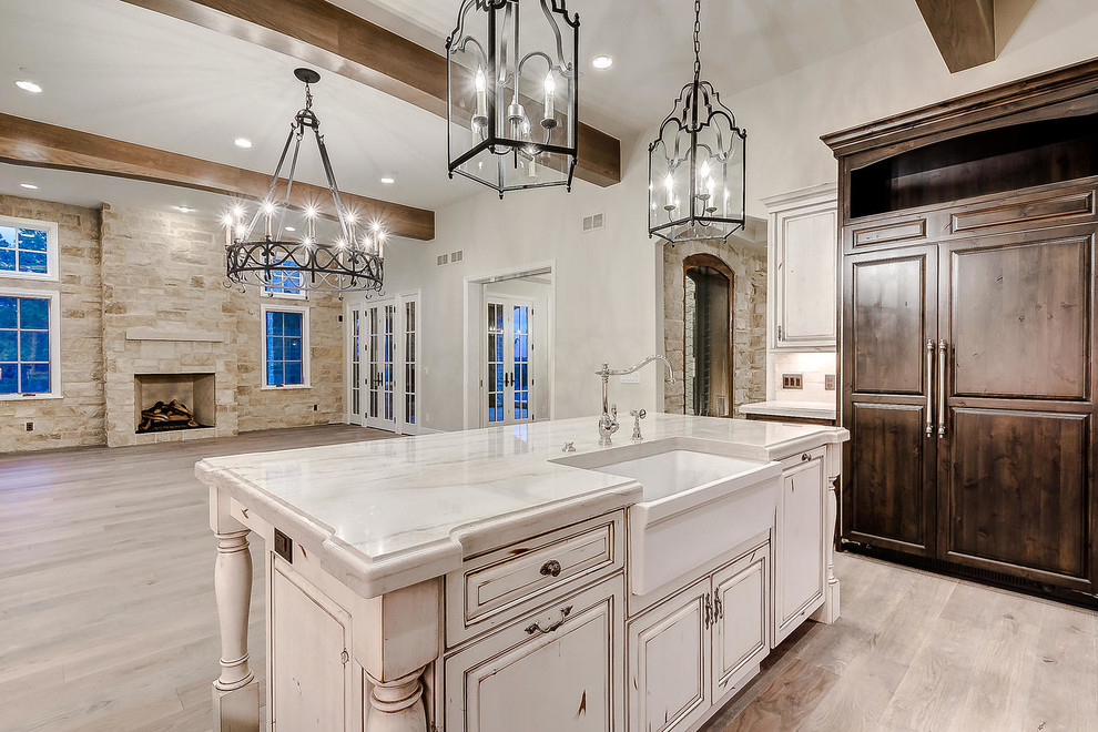 This is an example of a large u-shaped open plan kitchen in Denver with a farmhouse sink, raised-panel cabinets, distressed cabinets, marble benchtops, white splashback, stone tile splashback, stainless steel appliances, light hardwood floors, with island, brown floor and white benchtop.