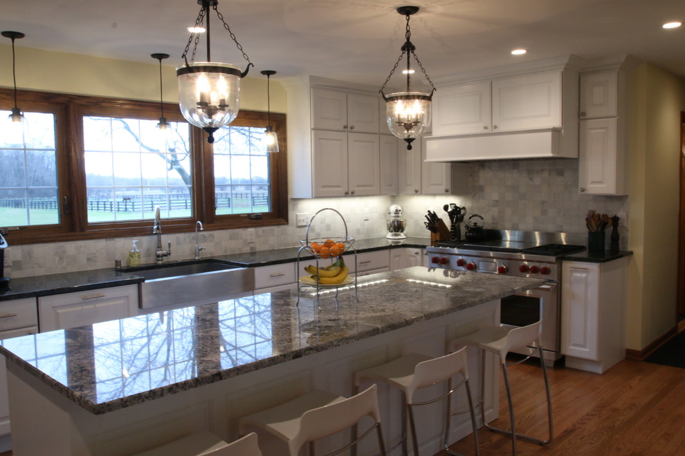 Photo of a large country l-shaped eat-in kitchen in Milwaukee with a farmhouse sink, raised-panel cabinets, white cabinets, granite benchtops, white splashback, marble splashback, stainless steel appliances, light hardwood floors, with island and brown floor.