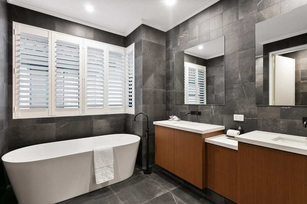 Inspiration for a contemporary master bathroom in Perth with flat-panel cabinets, medium wood cabinets, a freestanding tub, black tile, gray tile, marble, black walls, an undermount sink, black floor and white benchtops.