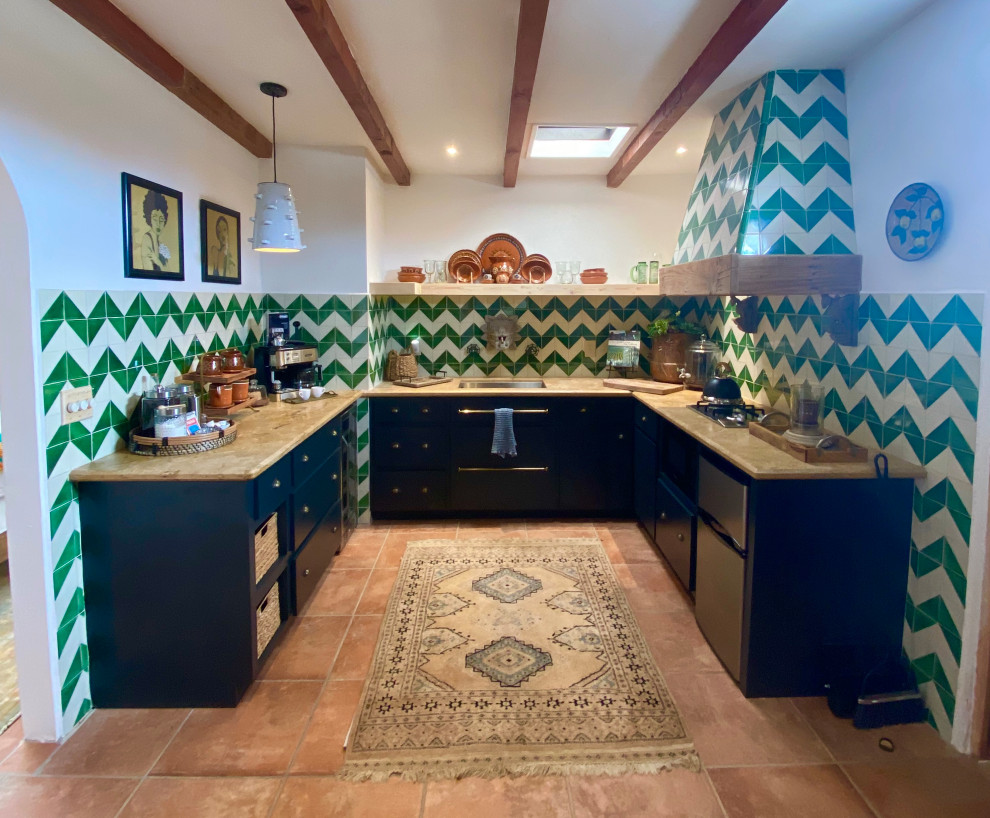 Inspiration for a mid-sized mediterranean u-shaped eat-in kitchen in San Diego with an undermount sink, flat-panel cabinets, black cabinets, marble benchtops, green splashback, terra-cotta splashback, stainless steel appliances, porcelain floors, orange floor, beige benchtop, exposed beam and no island.