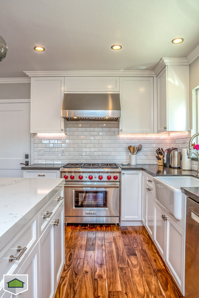 This is an example of a large contemporary u-shaped eat-in kitchen in San Francisco with a farmhouse sink, shaker cabinets, white cabinets, marble benchtops, white splashback, subway tile splashback, stainless steel appliances, medium hardwood floors and with island.