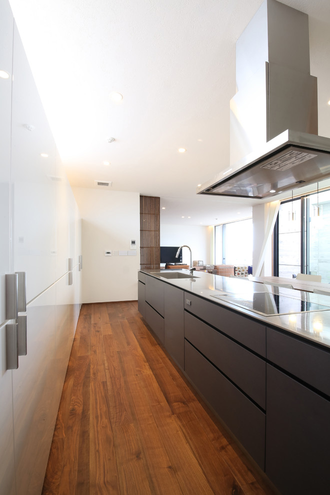 Mid-sized modern galley open plan kitchen in Other with an integrated sink, flat-panel cabinets, white cabinets, stainless steel benchtops, grey splashback, stone slab splashback and a peninsula.