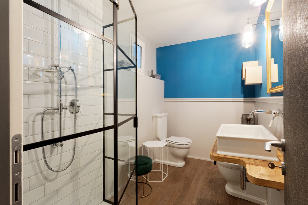Small eclectic powder room in Bologna with open cabinets, a two-piece toilet, white tile, blue walls, light hardwood floors, a vessel sink, wood benchtops, white benchtops, a floating vanity and wallpaper.