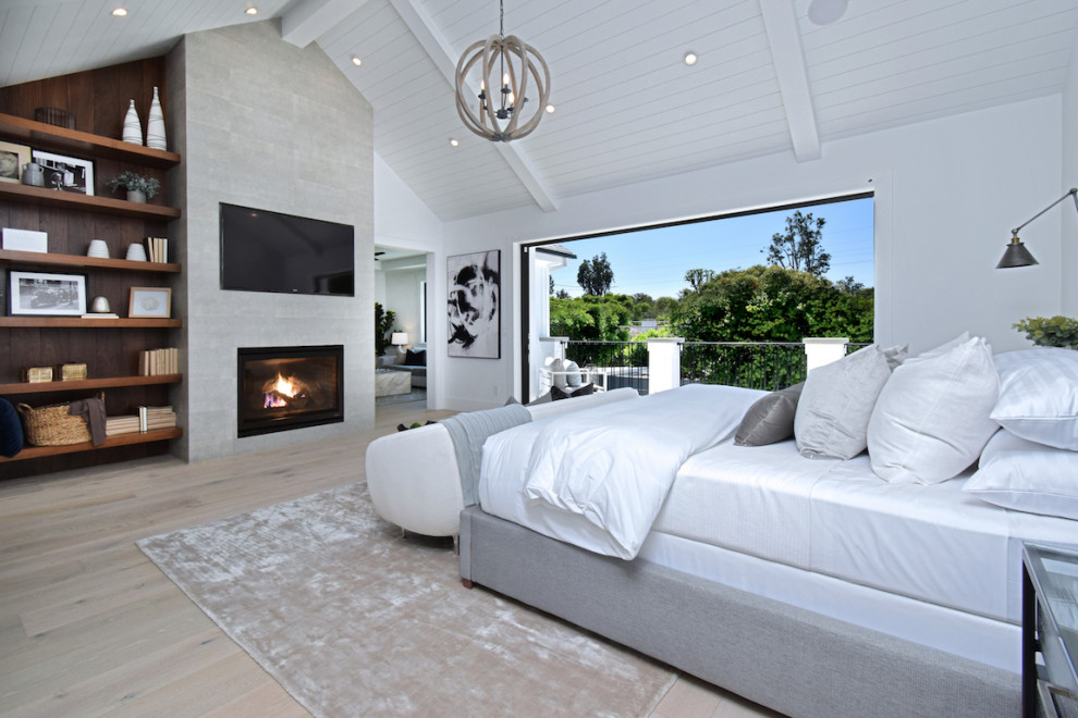 Photo of a large country master bedroom in Los Angeles with white walls, light hardwood floors, a standard fireplace, a tile fireplace surround, beige floor and wood.