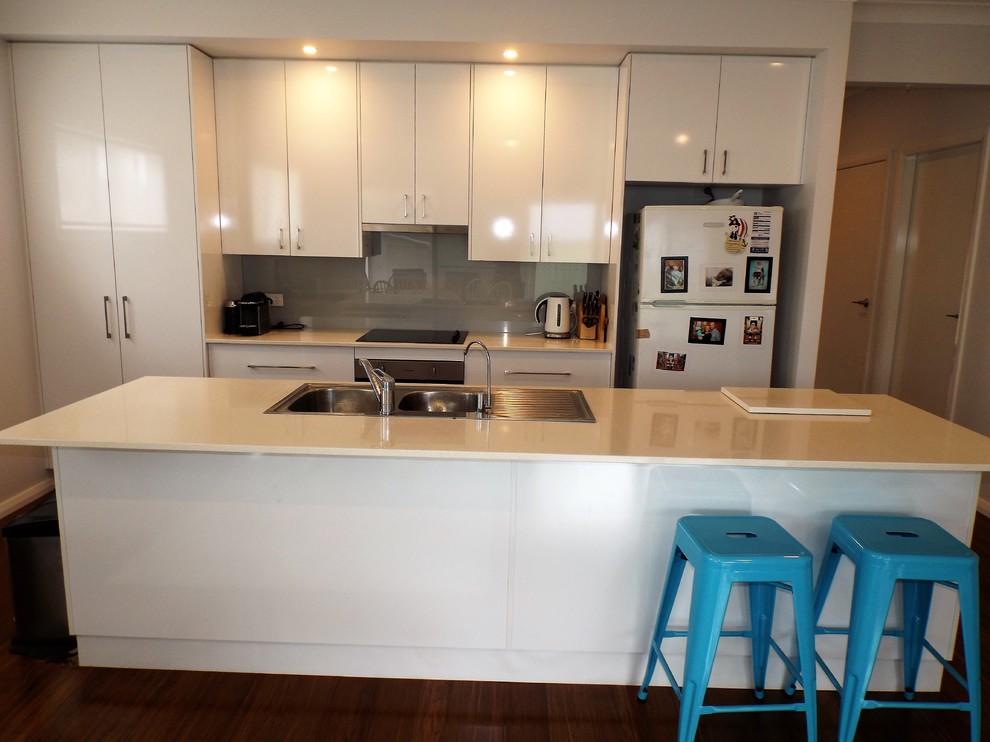 Photo of a small contemporary galley eat-in kitchen in Central Coast with a double-bowl sink, flat-panel cabinets, white cabinets, granite benchtops, grey splashback, glass sheet splashback, white appliances, bamboo floors and with island.