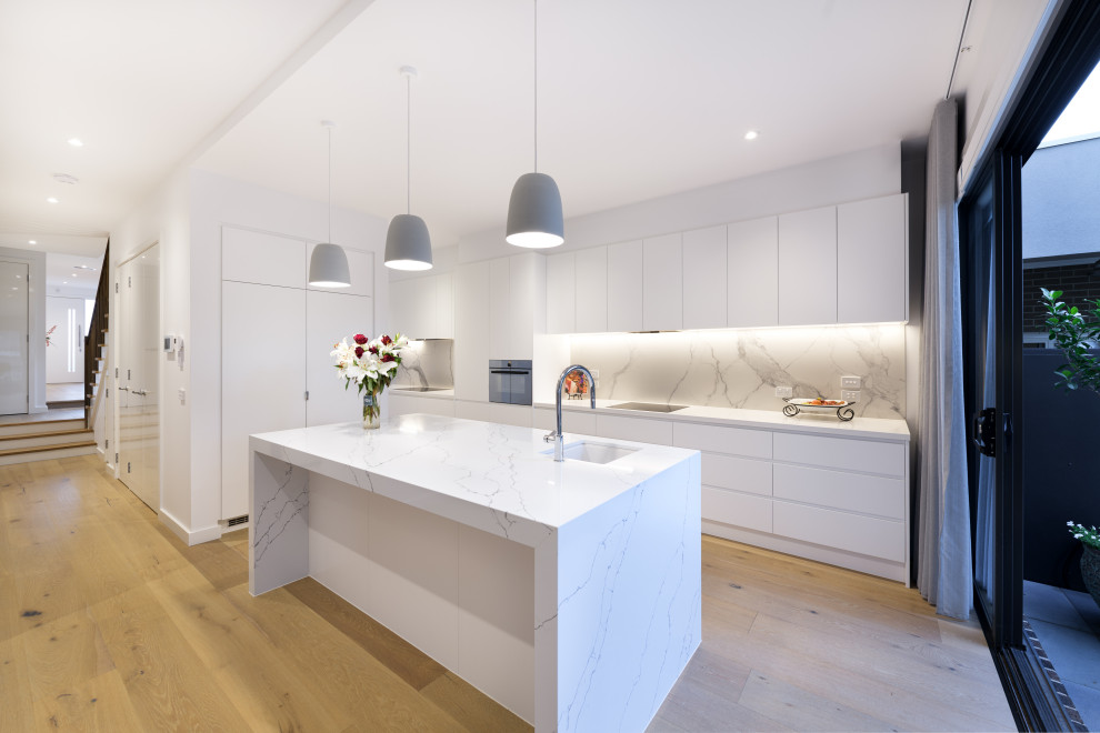 Large contemporary l-shaped kitchen in Melbourne with an undermount sink, flat-panel cabinets, white cabinets, grey splashback, panelled appliances, with island, beige floor and white benchtop.
