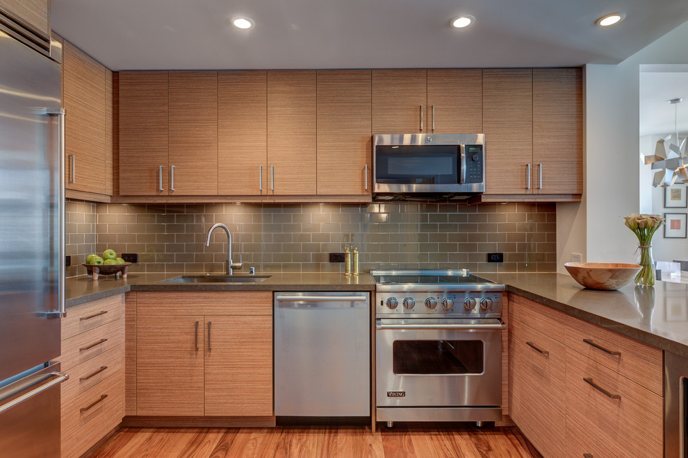 Photo of a small modern u-shaped eat-in kitchen in San Francisco with an undermount sink, flat-panel cabinets, medium wood cabinets, quartz benchtops, green splashback, glass tile splashback, stainless steel appliances, light hardwood floors and a peninsula.