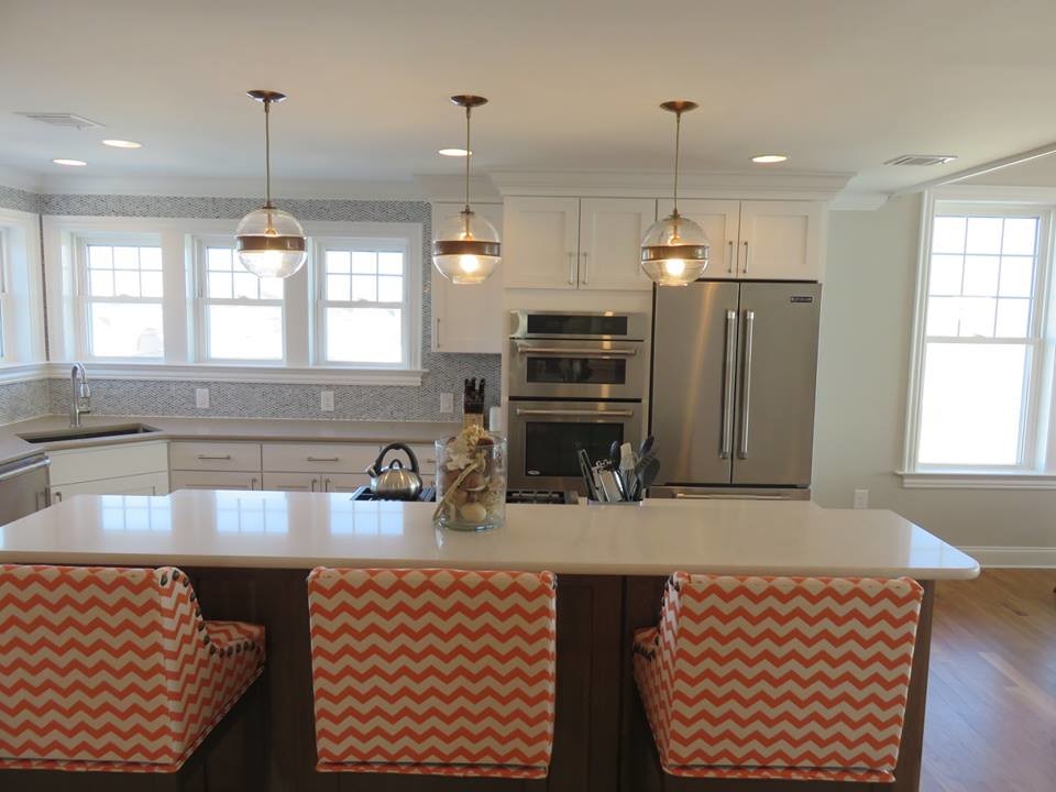 Photo of a large beach style l-shaped open plan kitchen in New York with recessed-panel cabinets, white cabinets, quartzite benchtops, stainless steel appliances, medium hardwood floors and with island.