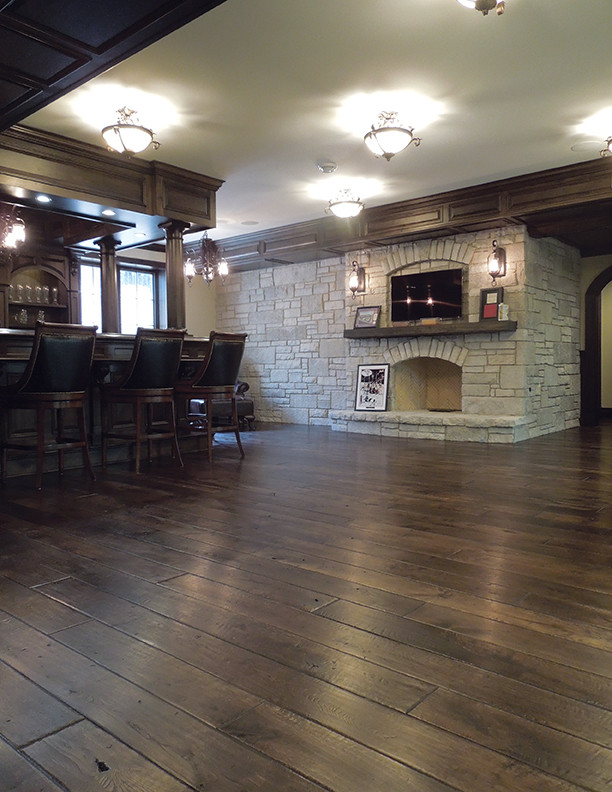 Imagen de salón con barra de bar tradicional grande con suelo de madera oscura, todas las chimeneas, marco de chimenea de piedra, televisor colgado en la pared y suelo marrón