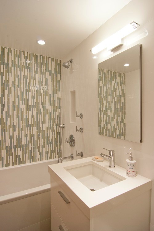 Photo of a small modern kids bathroom in New York with green tile, white walls, flat-panel cabinets, white cabinets, an alcove tub, a shower/bathtub combo, a one-piece toilet, mosaic tile, porcelain floors, an undermount sink, engineered quartz benchtops, white floor and a hinged shower door.