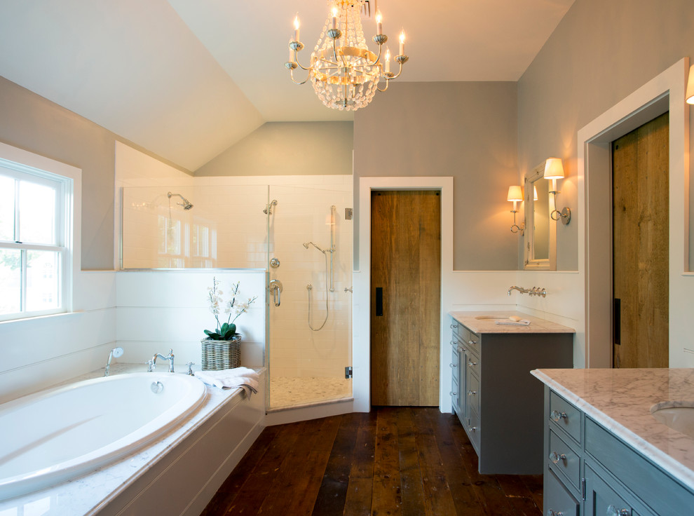 Photo of a mid-sized country master bathroom in Boston with a drop-in sink, marble benchtops, a drop-in tub, a corner shower, white tile, ceramic tile, grey walls, dark hardwood floors, beaded inset cabinets and grey cabinets.