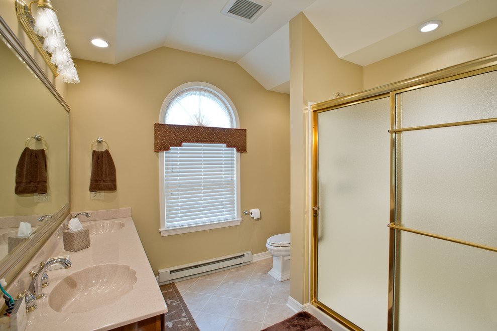 Mid-sized traditional master bathroom in Philadelphia with medium wood cabinets, an integrated sink, raised-panel cabinets, solid surface benchtops, an alcove shower, a two-piece toilet, white tile, ceramic tile, beige walls and ceramic floors.