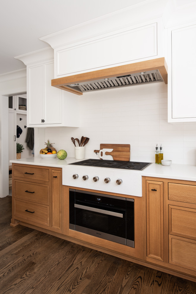 This is an example of a mid-sized transitional l-shaped eat-in kitchen in New York with a drop-in sink, beaded inset cabinets, white cabinets, solid surface benchtops, white splashback, porcelain splashback, medium hardwood floors, with island and white benchtop.