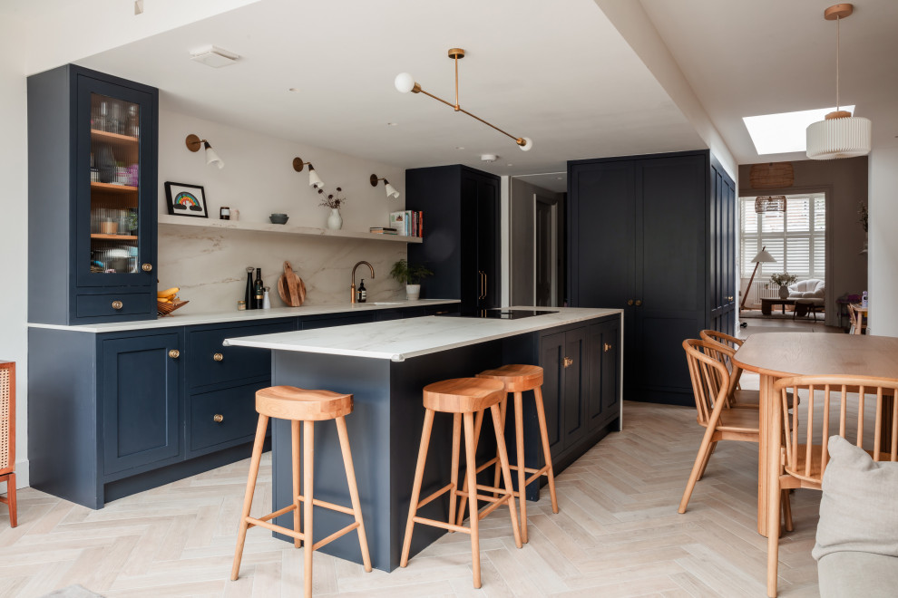 Mid-sized transitional u-shaped eat-in kitchen in London with an undermount sink, shaker cabinets, grey cabinets, quartzite benchtops, white splashback, granite splashback, black appliances, medium hardwood floors, with island, brown floor and white benchtop.