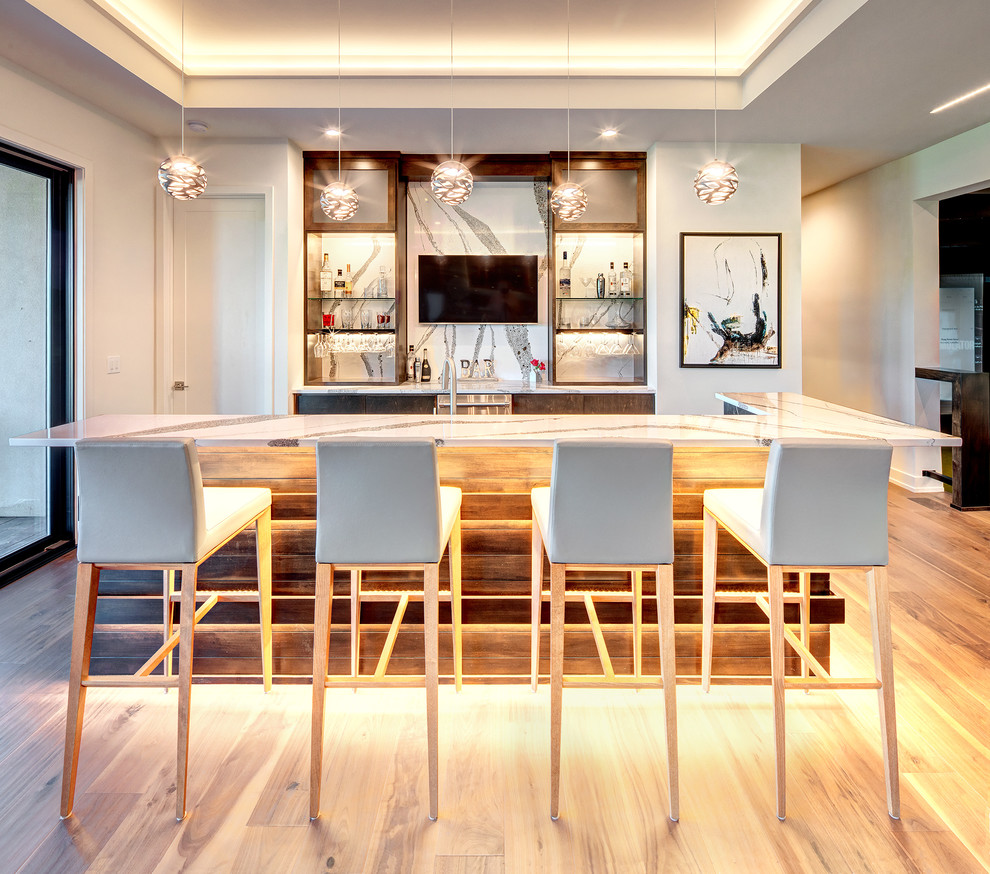 This is an example of a contemporary galley seated home bar in Dallas with flat-panel cabinets, dark wood cabinets, white splashback, light hardwood floors, beige floor and white benchtop.