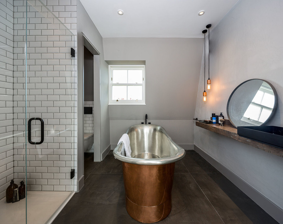 This is an example of a mid-sized contemporary master bathroom in London with a freestanding tub, an open shower, a wall-mount toilet, brown tile, stone tile, white walls, cement tiles and a trough sink.