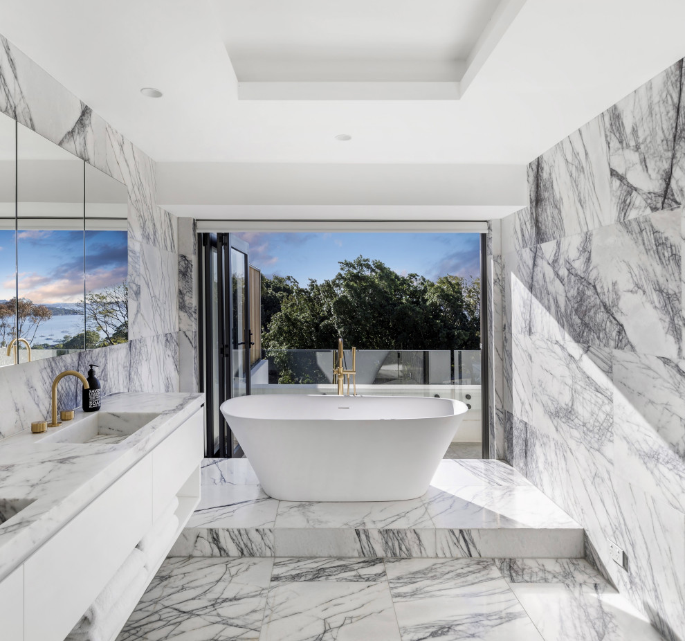 На фото: главная ванная комната в современном стиле с плоскими фасадами, белыми фасадами, отдельно стоящей ванной, белой плиткой, монолитной раковиной, белым полом, белой столешницей, тумбой под две раковины и подвесной тумбой