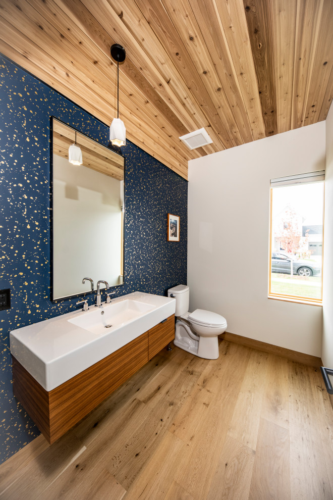Large contemporary powder room in Other with flat-panel cabinets, brown cabinets, a one-piece toilet, blue walls, light hardwood floors, an integrated sink, engineered quartz benchtops, white floor, white benchtops, a floating vanity, wood and wallpaper.