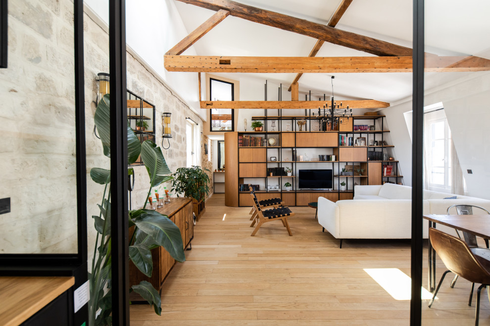 Modernes Wohnzimmer mit weißer Wandfarbe, hellem Holzboden, freistehendem TV, freigelegten Dachbalken und Steinwänden in Paris