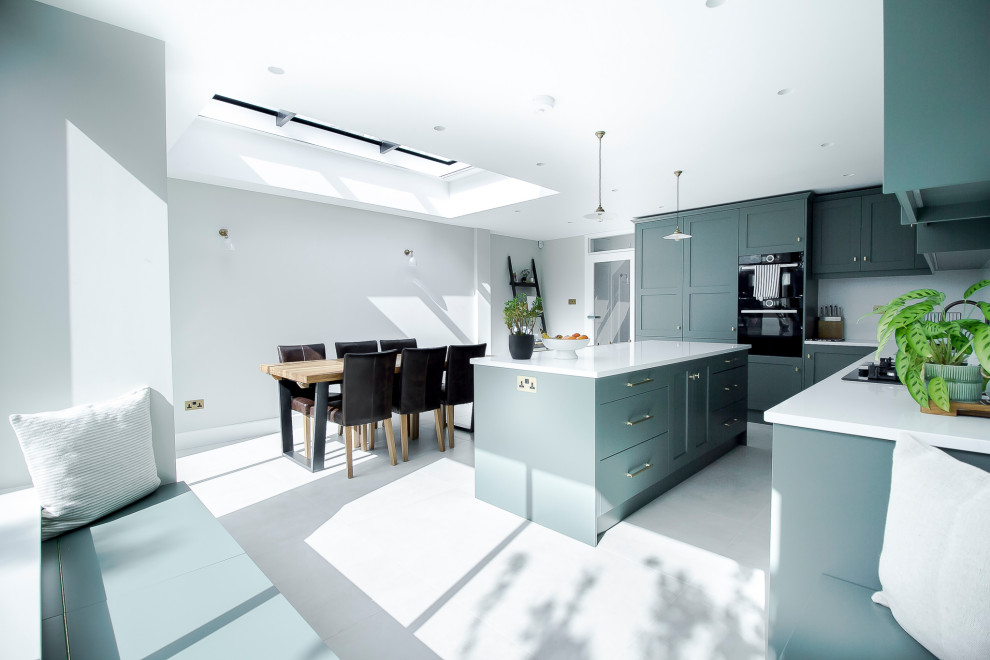 Mid-sized modern l-shaped open plan kitchen in Surrey with an integrated sink, shaker cabinets, green cabinets, quartzite benchtops, white splashback, limestone splashback, panelled appliances, concrete floors, a peninsula, grey floor and white benchtop.