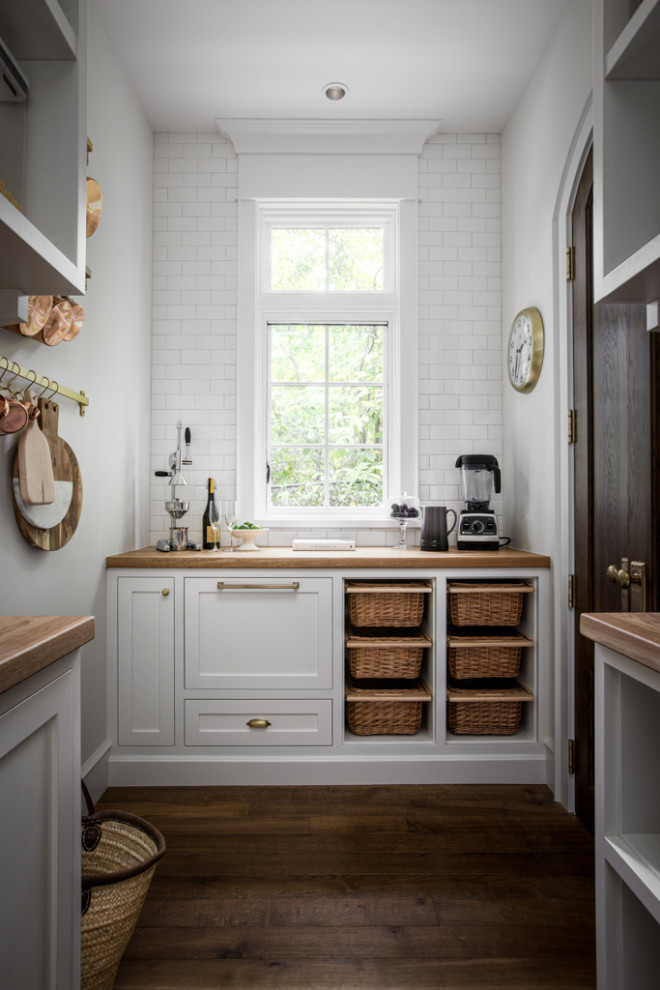 Large transitional u-shaped medium tone wood floor and brown floor kitchen pantry photo with a farmhouse sink, shaker cabinets, white cabinets, marble countertops, white backsplash, subway tile backsplash, paneled appliances, an island and white countertops