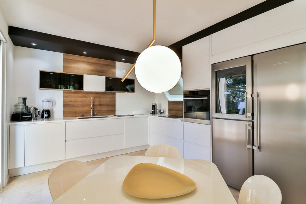 Photo of a mid-sized contemporary l-shaped open plan kitchen in Marseille with an undermount sink, glass-front cabinets, white cabinets, white splashback, timber splashback, stainless steel appliances, travertine floors, no island and white benchtop.