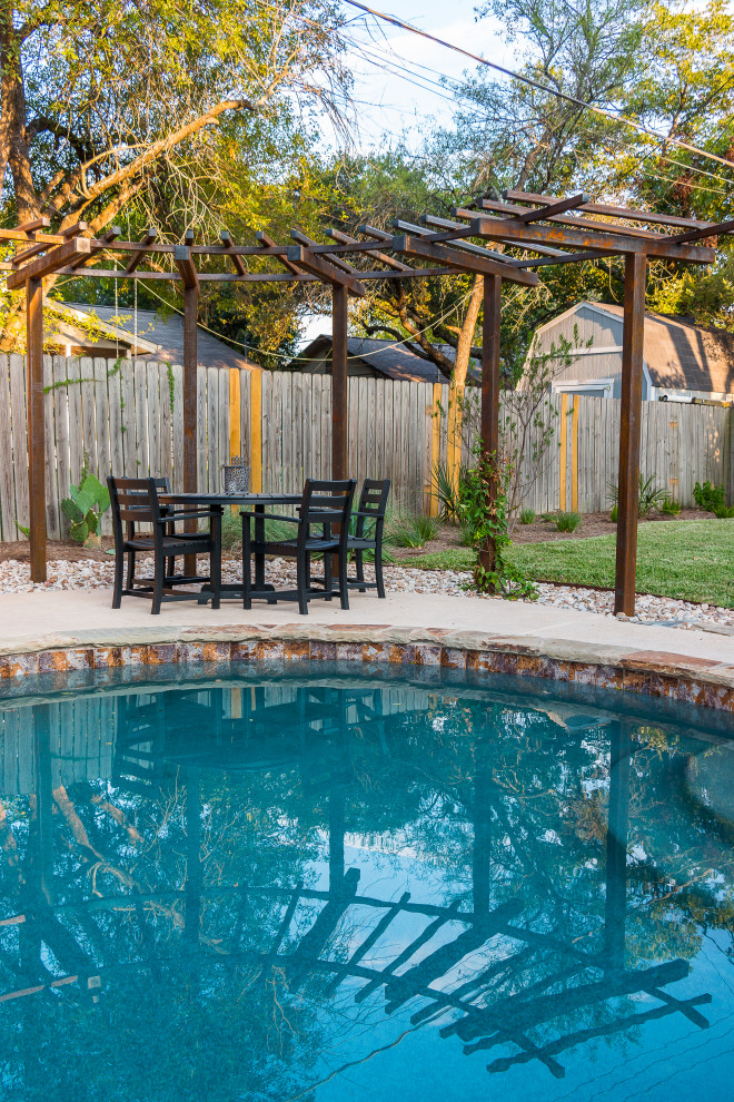 This is an example of a mid-sized and desert look contemporary backyard partial sun xeriscape for summer in Austin with a wood fence and river rock.