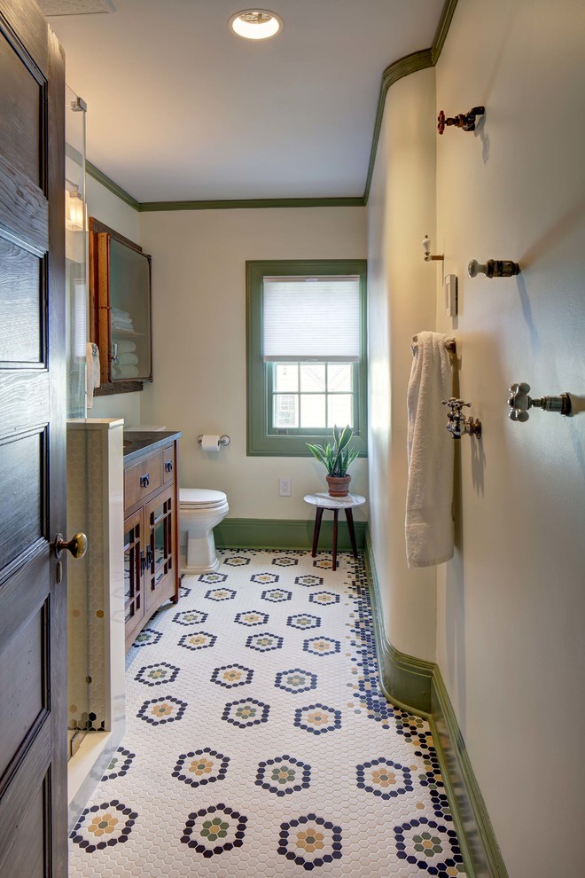 Photo of a mid-sized arts and crafts bathroom in New York with furniture-like cabinets, medium wood cabinets, a two-piece toilet, white tile, white walls, porcelain floors, an undermount sink, granite benchtops, multi-coloured floor, a hinged shower door and grey benchtops.