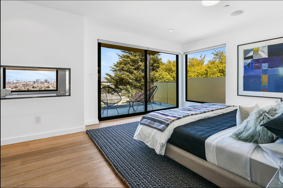 This is an example of a modern master bedroom in San Francisco with light hardwood flooring, a two-sided fireplace and a metal fireplace surround.