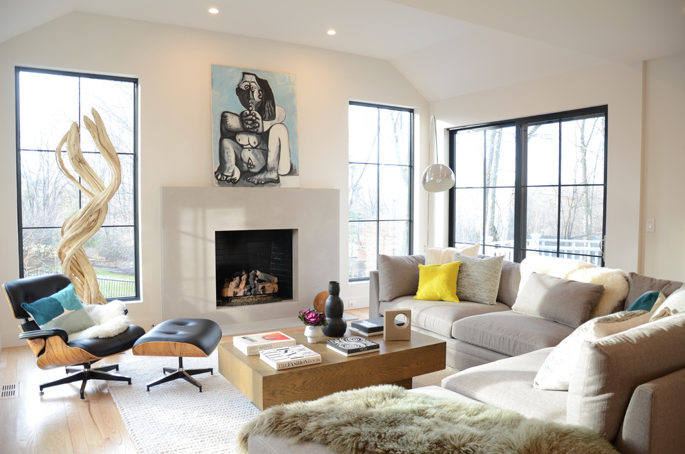 Photo of a large contemporary open concept living room in New York with grey walls, a standard fireplace, a concrete fireplace surround, light hardwood floors and beige floor.