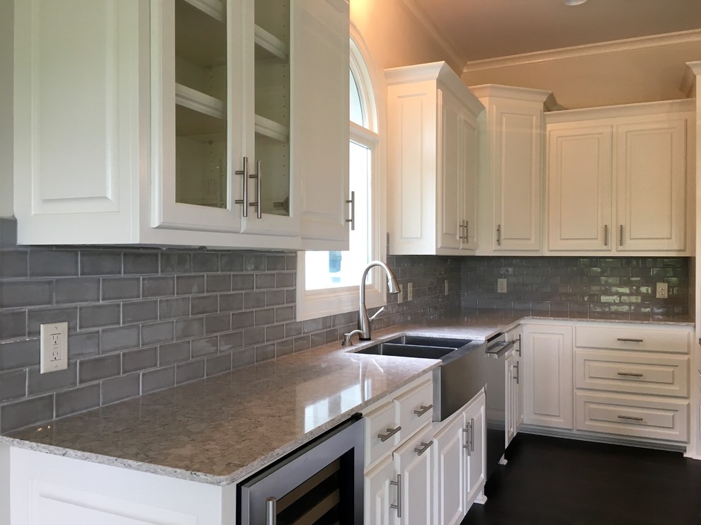 Large transitional u-shaped dark wood floor enclosed kitchen photo in New Orleans with a farmhouse sink, raised-panel cabinets, white cabinets, quartzite countertops, gray backsplash, subway tile backsplash, stainless steel appliances and an island