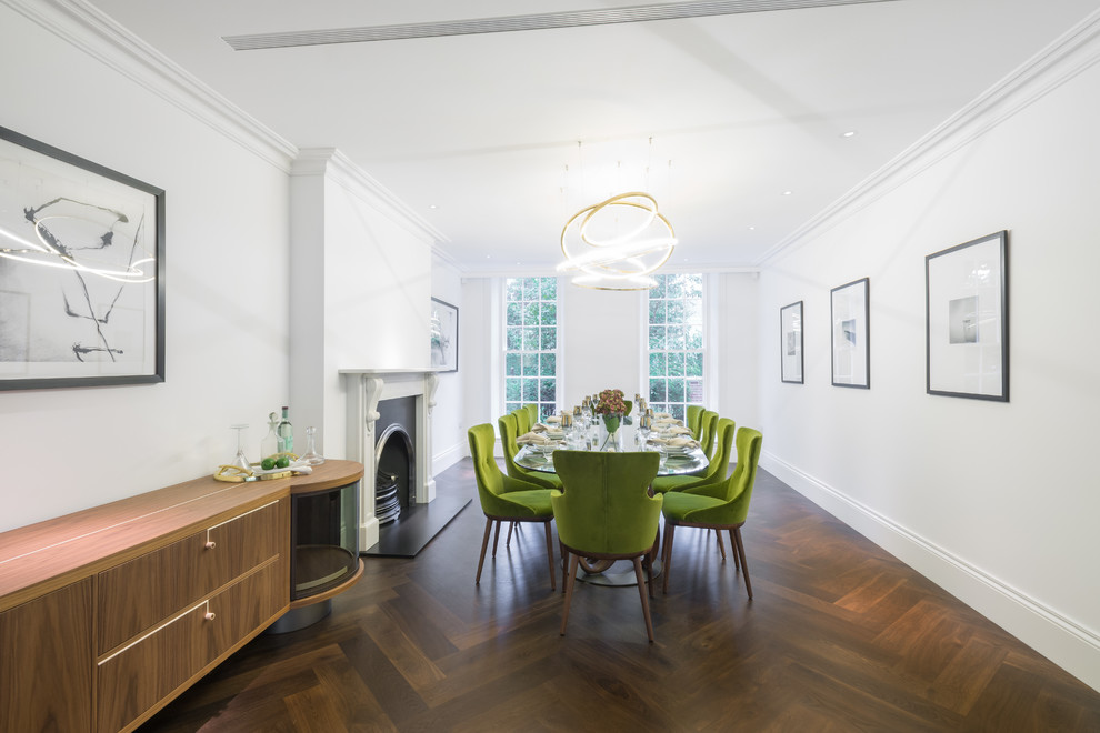 This is an example of a contemporary dining room in London with white walls, dark hardwood floors, a standard fireplace and brown floor.