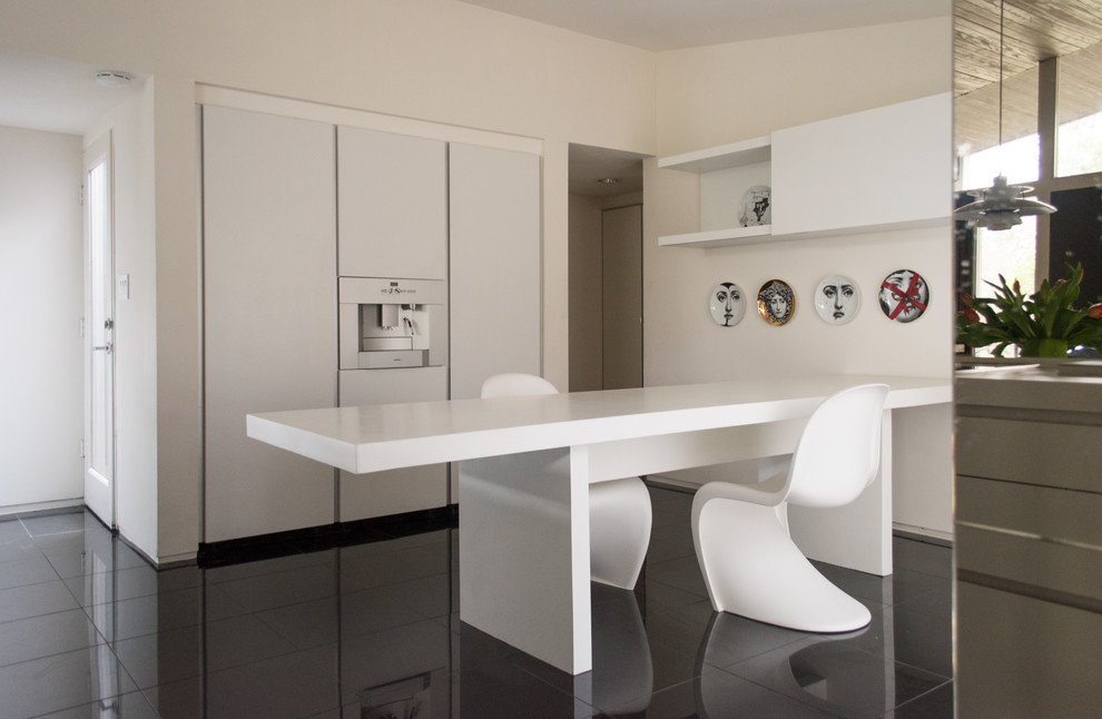 Photo of a midcentury kitchen in Dallas with flat-panel cabinets, white cabinets, a peninsula and black floor.