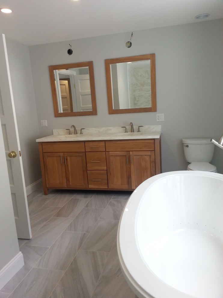 Mid-sized transitional master bathroom in Boston with recessed-panel cabinets, medium wood cabinets, a freestanding tub, a two-piece toilet, grey walls, ceramic floors, an undermount sink, granite benchtops and grey floor.