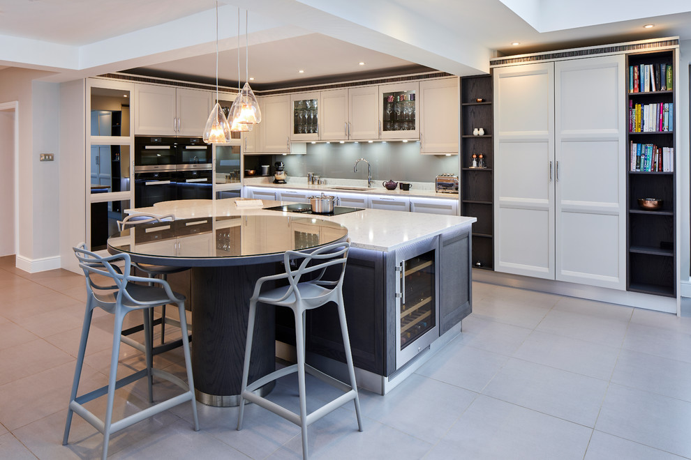 Mid-sized modern l-shaped open plan kitchen in Surrey with black splashback, black appliances, medium hardwood floors, with island and beige benchtop.