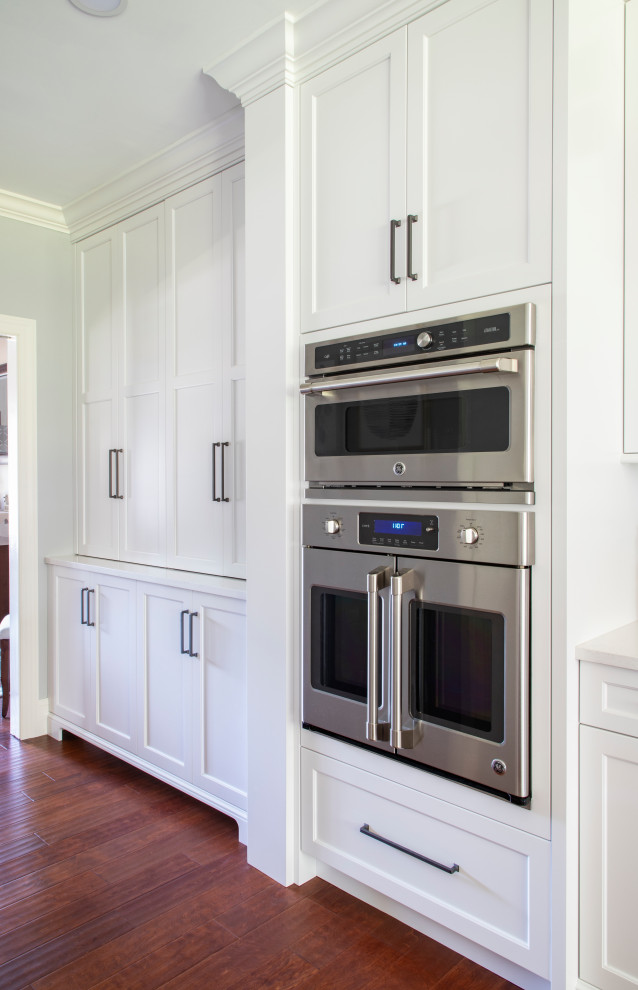Transitional medium tone wood floor kitchen photo with an undermount sink, shaker cabinets, quartz countertops, gray backsplash, porcelain backsplash, stainless steel appliances, an island and white countertops