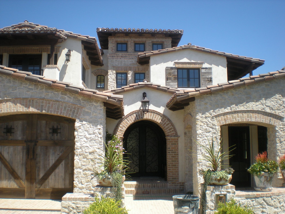Photo of an expansive mediterranean three-storey beige house exterior in Orange County with mixed siding, a clipped gable roof and a tile roof.