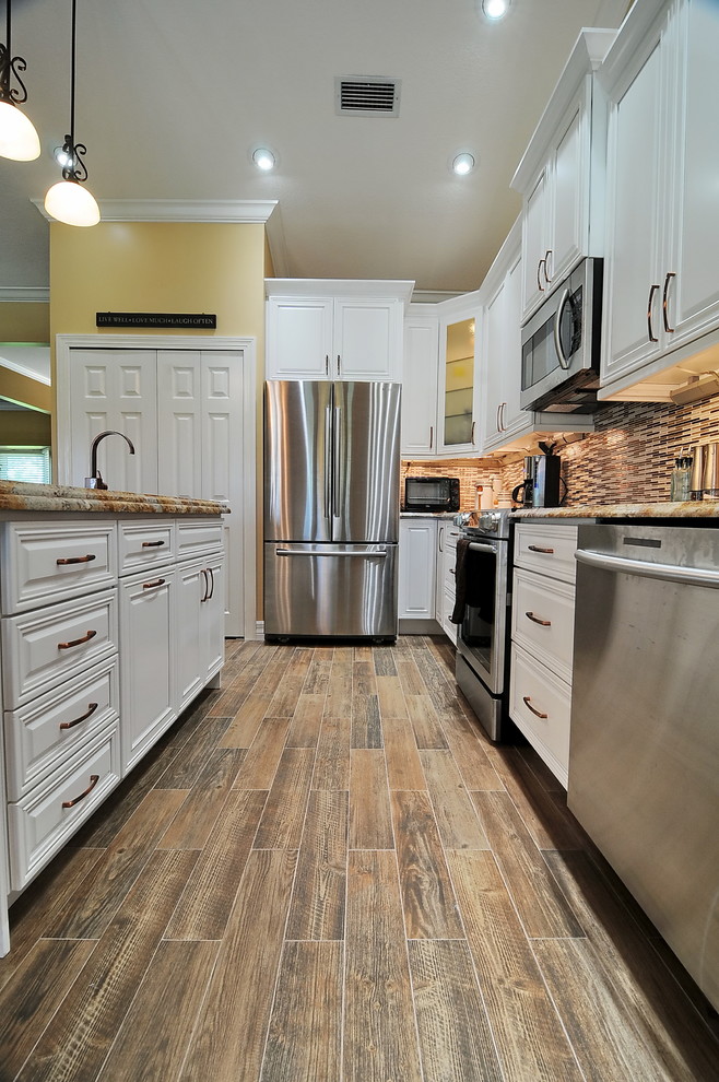 Example of a transitional medium tone wood floor kitchen design in Miami with a farmhouse sink, raised-panel cabinets, white cabinets, granite countertops, ceramic backsplash, stainless steel appliances and an island